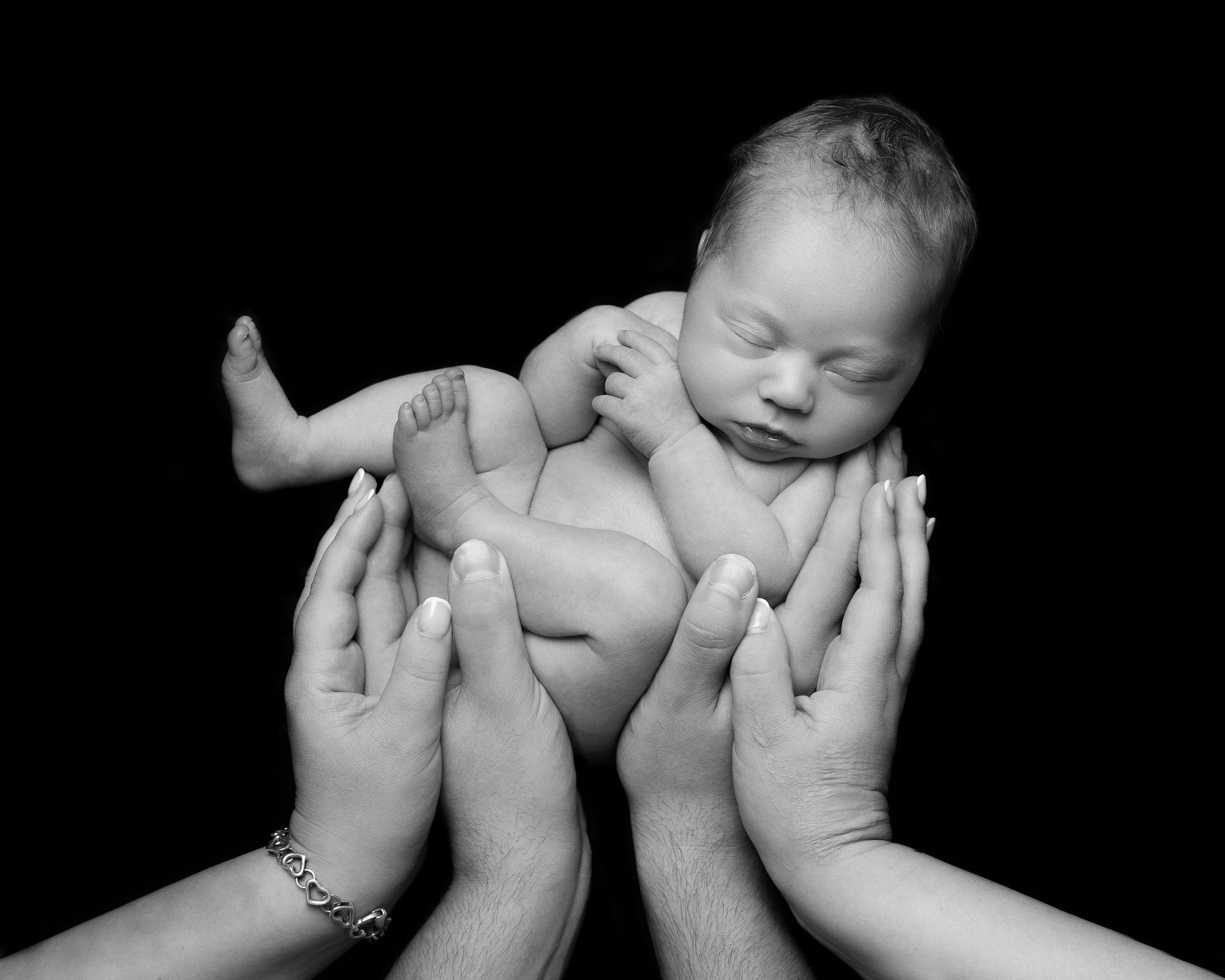 Newborn baby cradled in hands, sleeping peacefully against a black background.