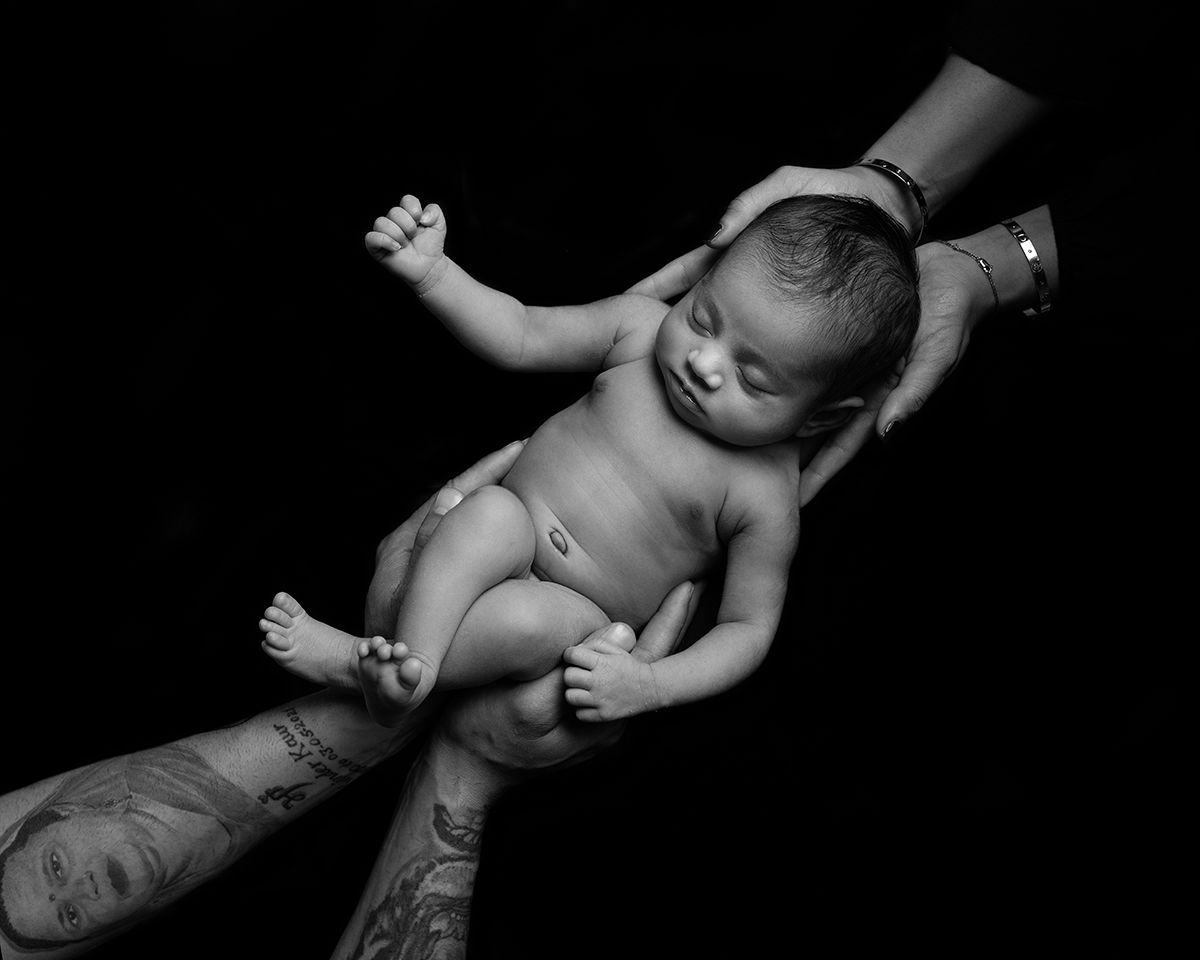 Newborn baby held in hands of adults, black and white photo.