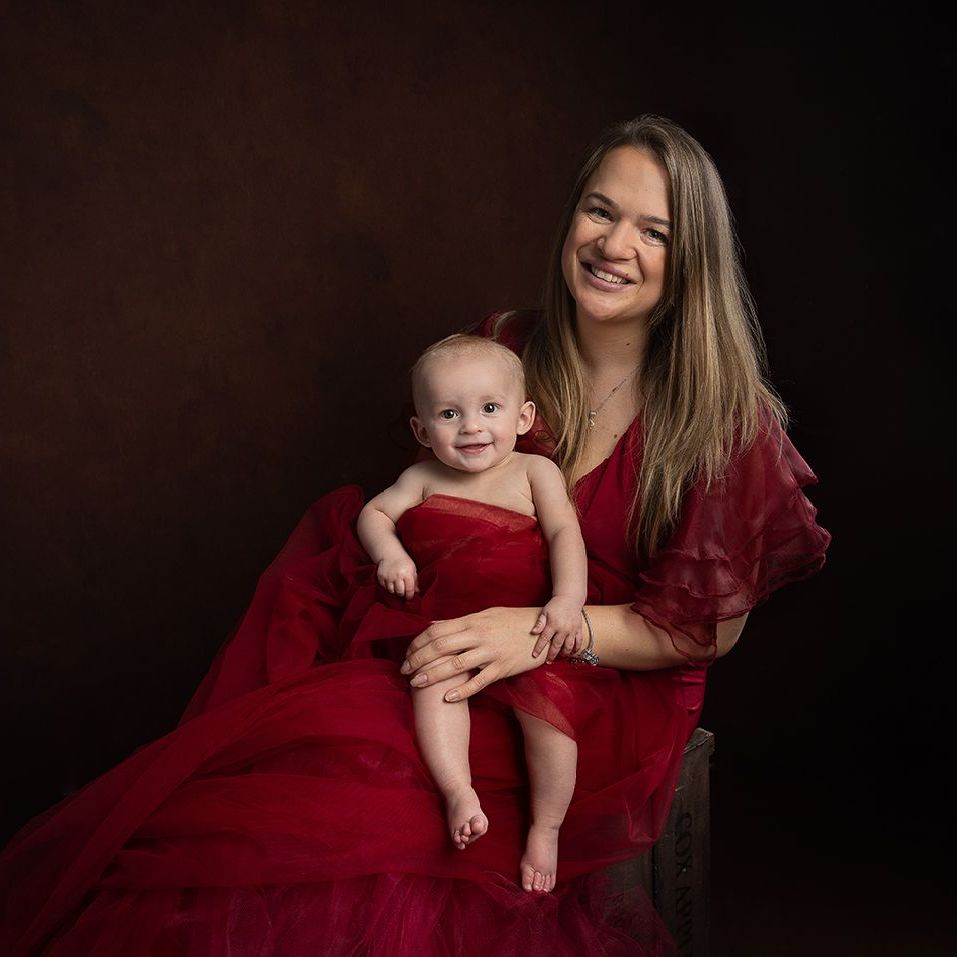 A woman in a red dress is holding a baby in her lap.