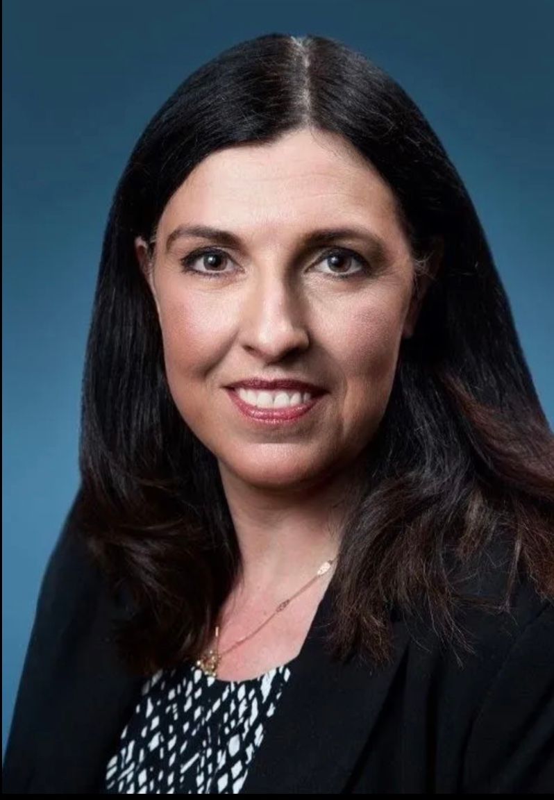 A woman with long dark hair is smiling and wearing a black jacket.