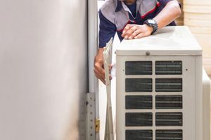 A man is working on an air conditioner outside of a building.