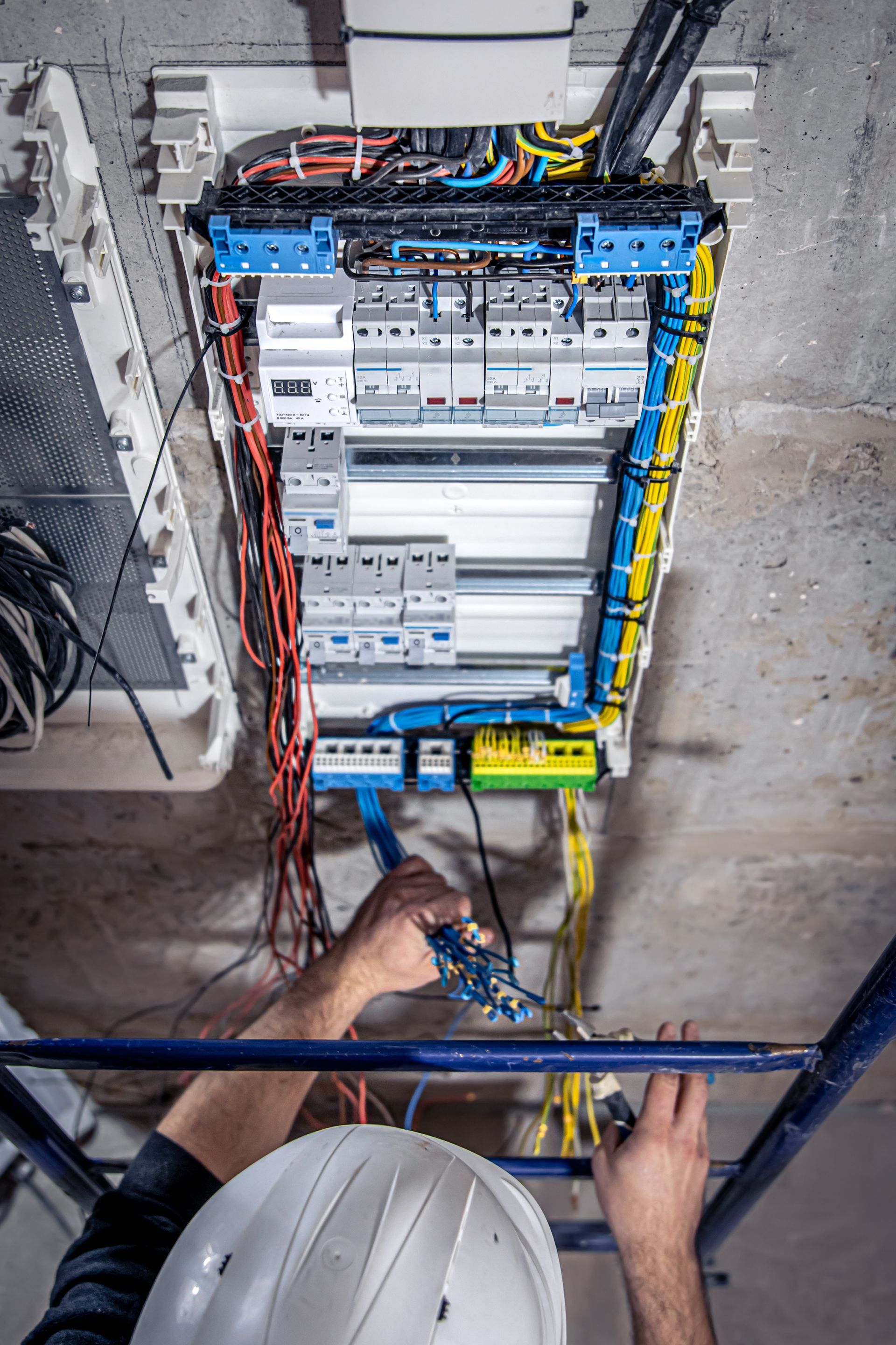 A man is working on an electrical box on a ladder.