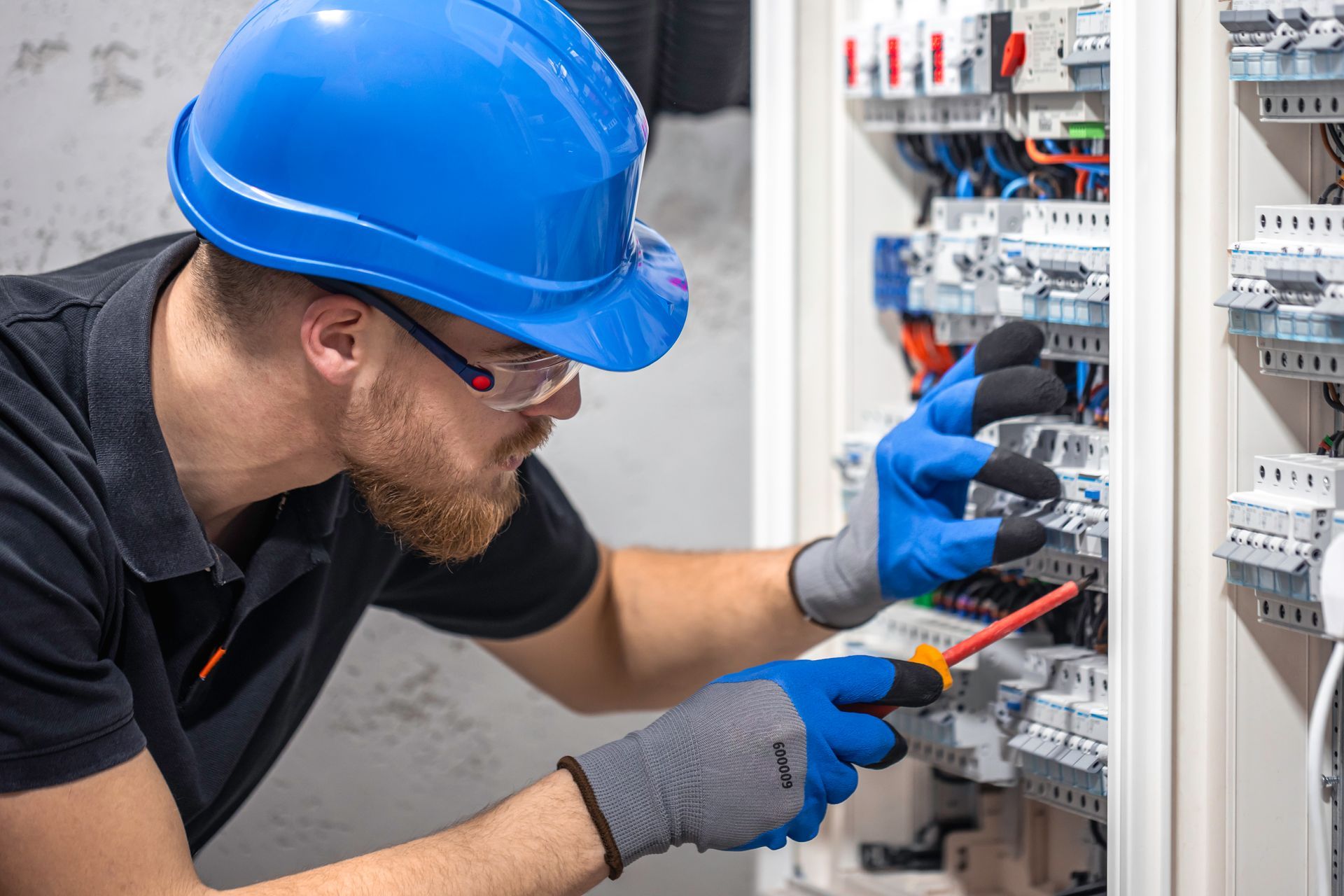 A man wearing a hard hat and gloves is working on an electrical box.