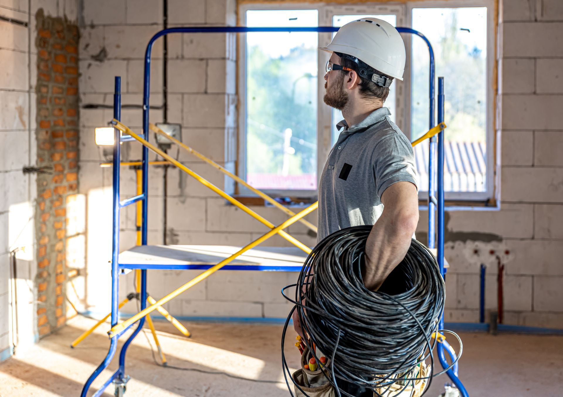 A man is standing on a scaffolding holding a roll of wires.