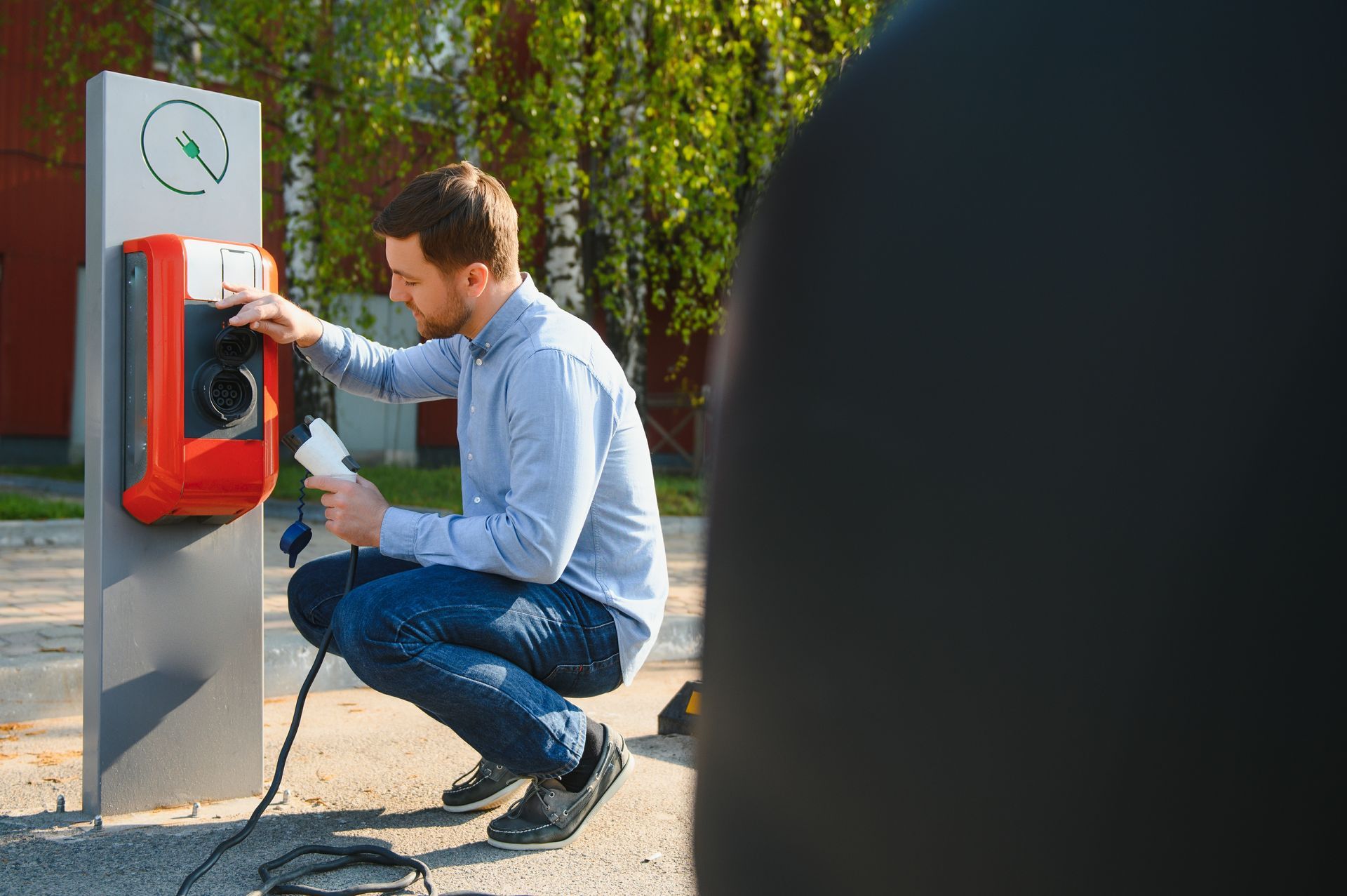 A man is kneeling down to charge an electric car at a charging station.