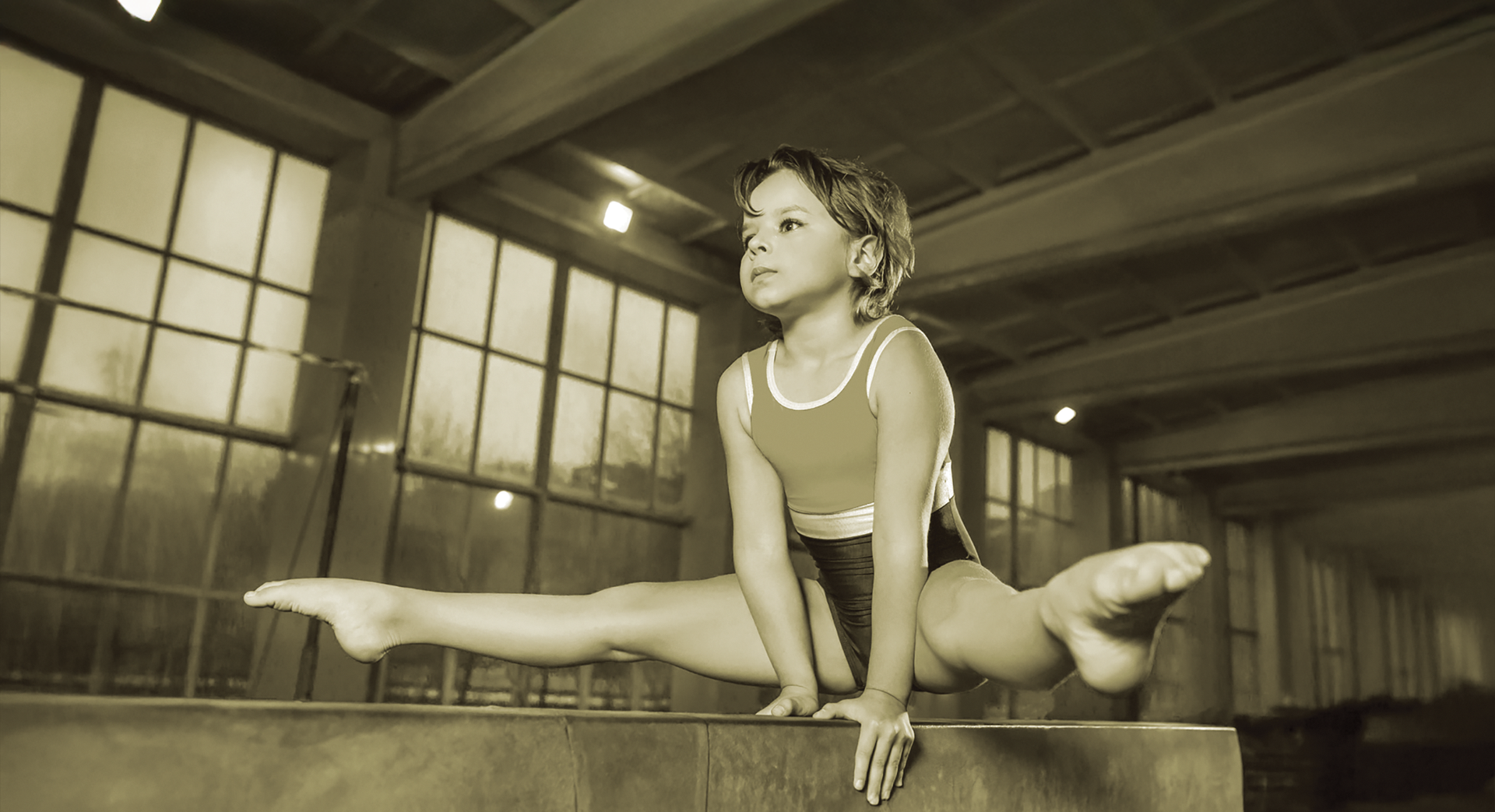 Gymnast on balance beam, split, sepia tone, focused expression.