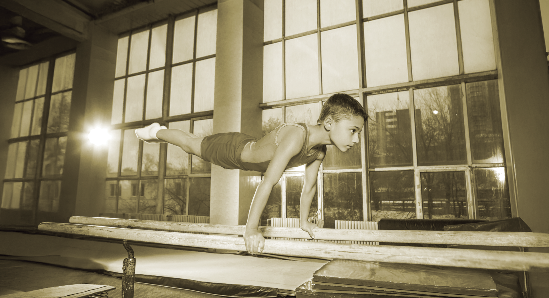 Boy doing a handstand on a beam in a gymnasium; sepia tone.