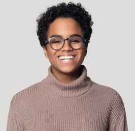 Woman with short, curly dark hair, wearing glasses and a tan turtleneck, smiling at the camera.