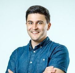 Man with crossed arms smiling, wearing a blue button-down shirt against a white backdrop.