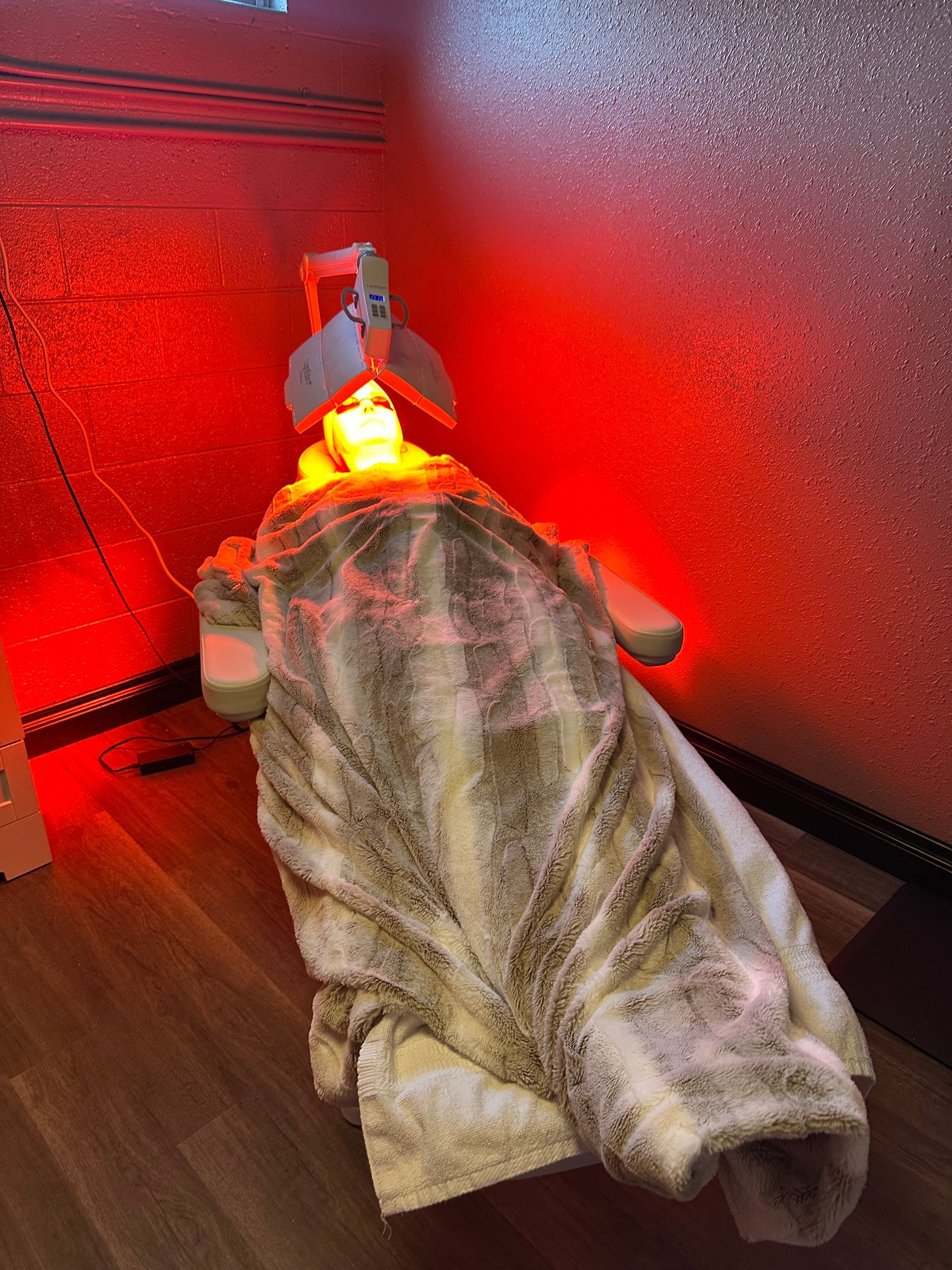 A person is laying on a bed with a blanket and a red light on their head.