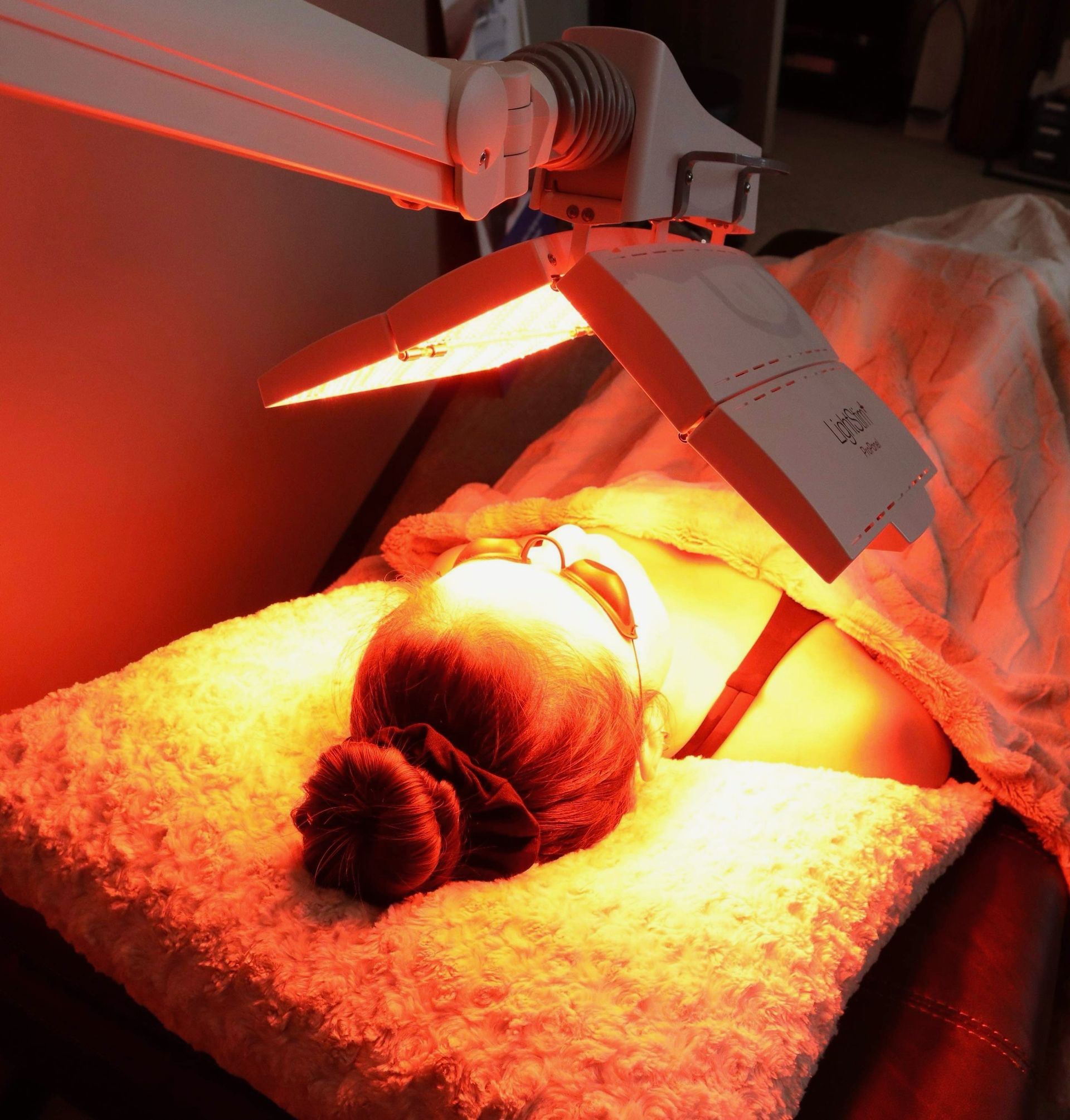 A woman is laying on a bed with a light on her face