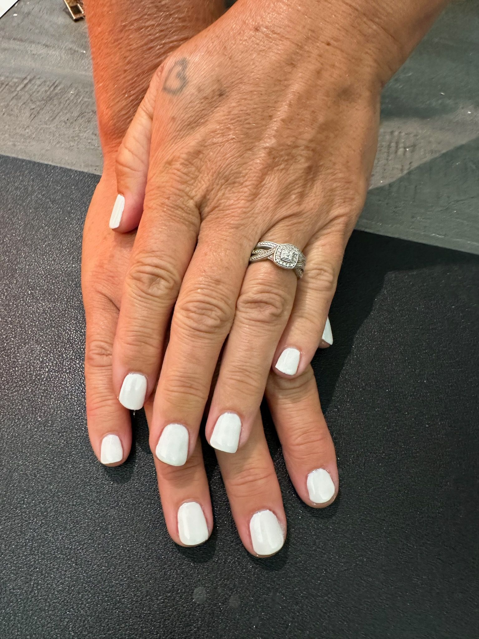 A woman 's hand with white nails and a ring on her finger.