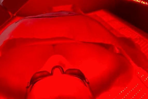 A person is laying in a bed with red lights on their face.