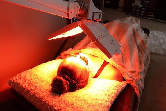 A woman is laying on a bed with a red light on her face.