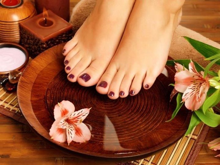 A woman 's feet are sitting on a wooden plate surrounded by flowers and candles.