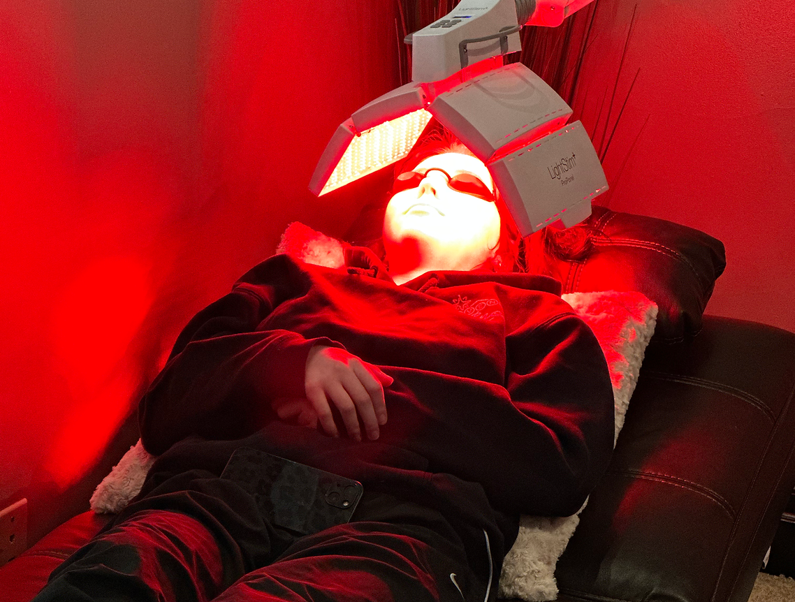 A person is laying on a bed with a red light on their face.