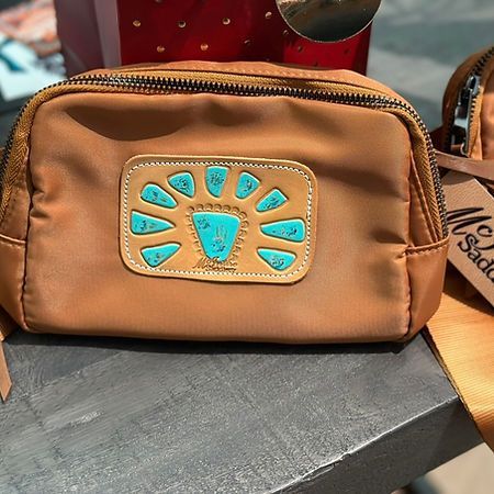 A brown purse with a turquoise design on it is sitting on a table.