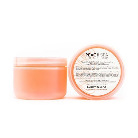 A jar of peach spa sugar scrub is sitting on a white surface.