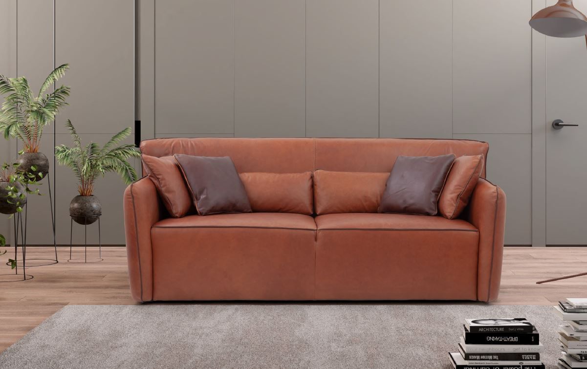 Ein braunes Ledersofa steht in einem Wohnzimmer neben einem Stapel Bücher.