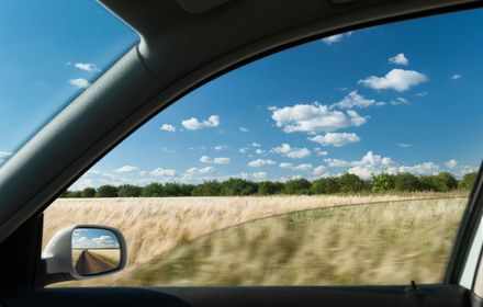 A car is driving down a road with a field in the background