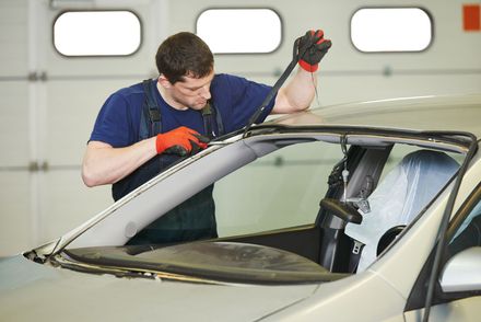 A man in a blue shirt is working on a car windshield