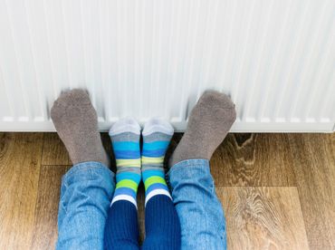 A man and a child in winter socks warm their feet near the heater.