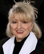 A woman in a black jacket and white collar is smiling for the camera.