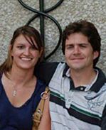 A man and a woman are posing for a picture in front of a stone wall.