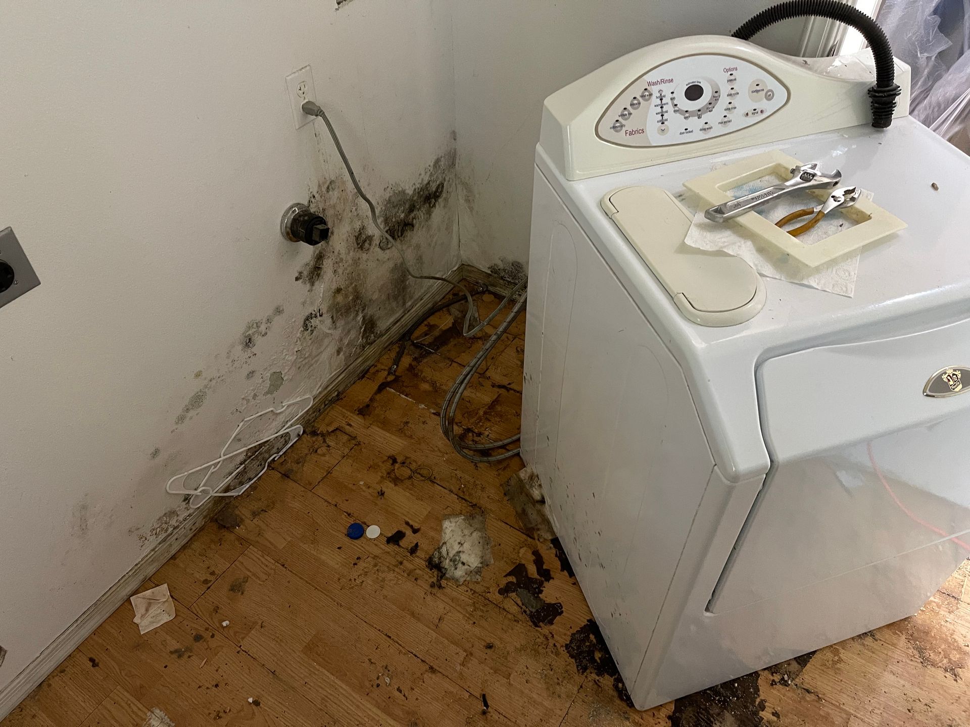 A washer and dryer are sitting on a wooden floor in a dirty room.