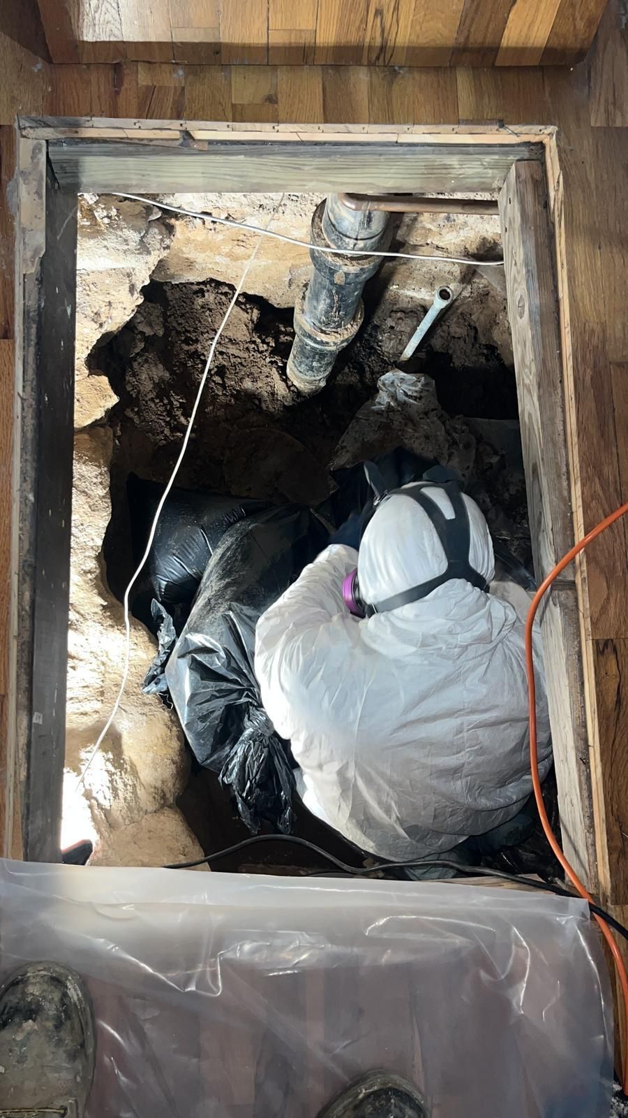 A man in a protective suit is crawling through a hole in the ground.