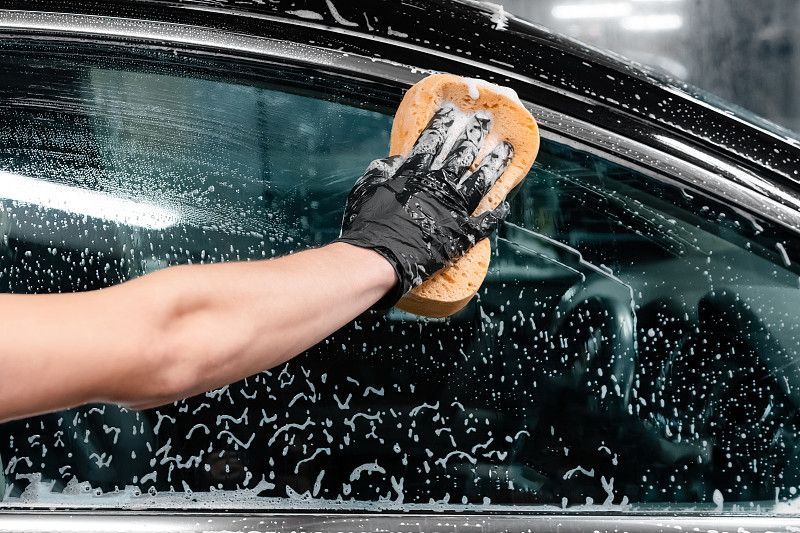 Hand washing a car window with a sponge and soap suds