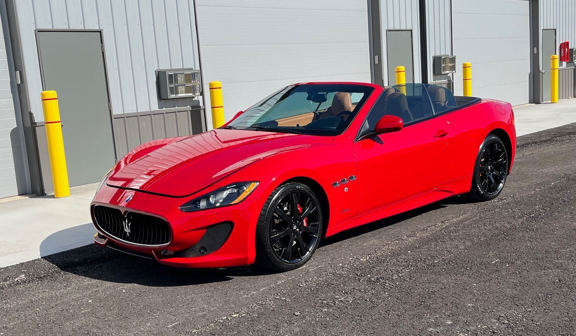 A red maserati granturismo convertible is parked in front of a building.