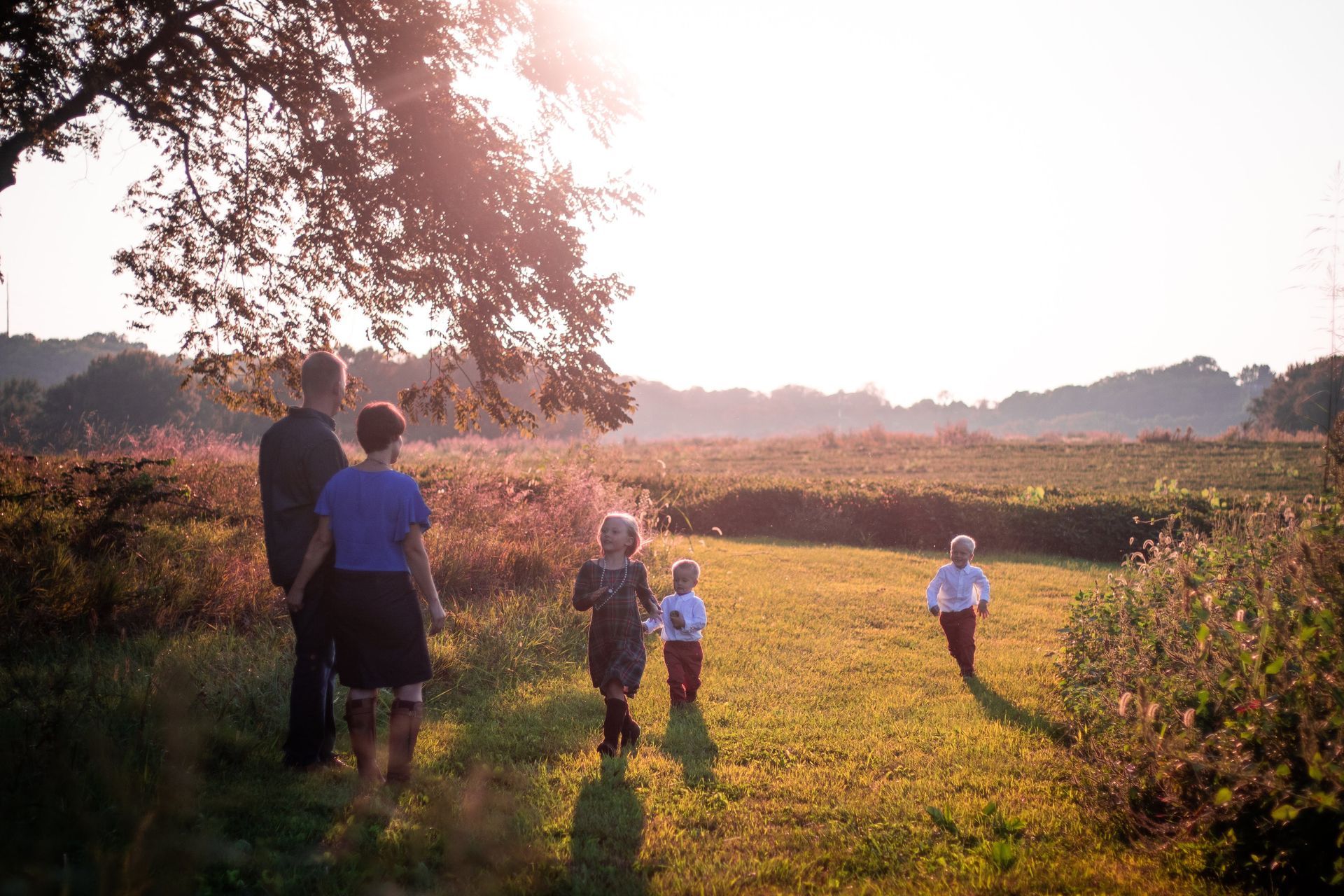 A family is walking through a grassy field at sunset.