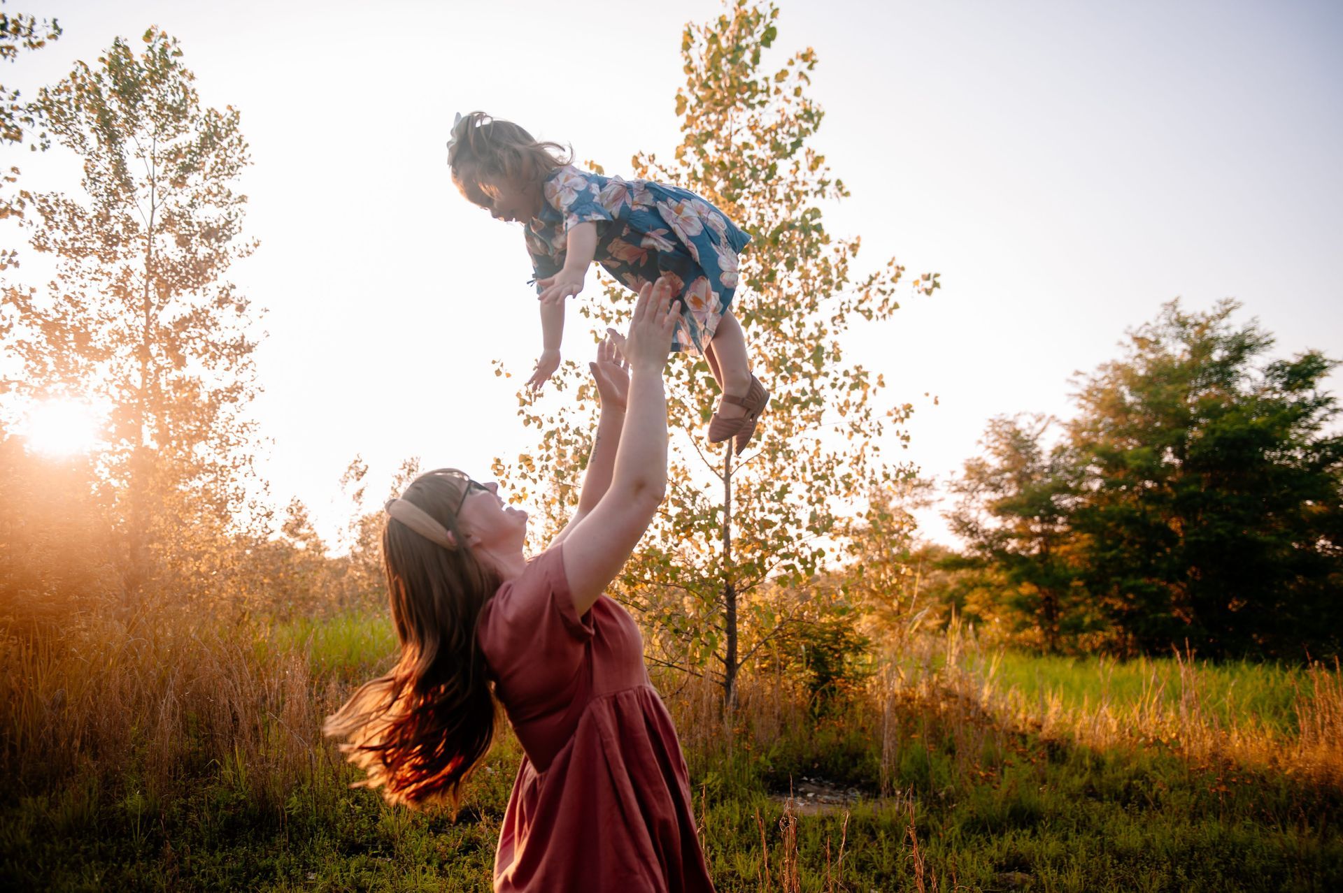 A woman is holding a little girl in the air in a field.
