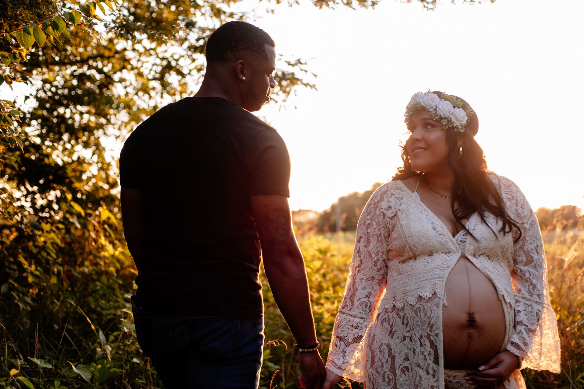 A man and a pregnant woman are holding hands in a field.