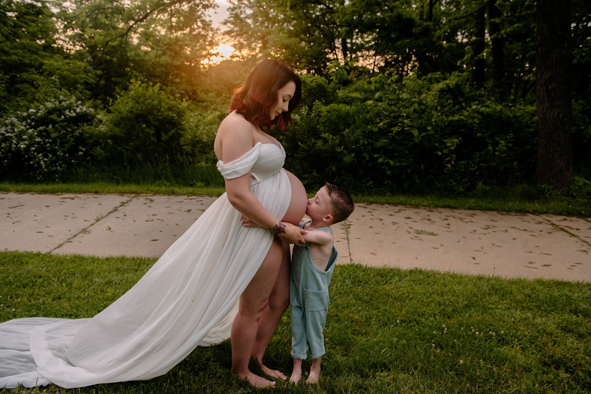 A pregnant woman in a white dress is standing next to a little boy.