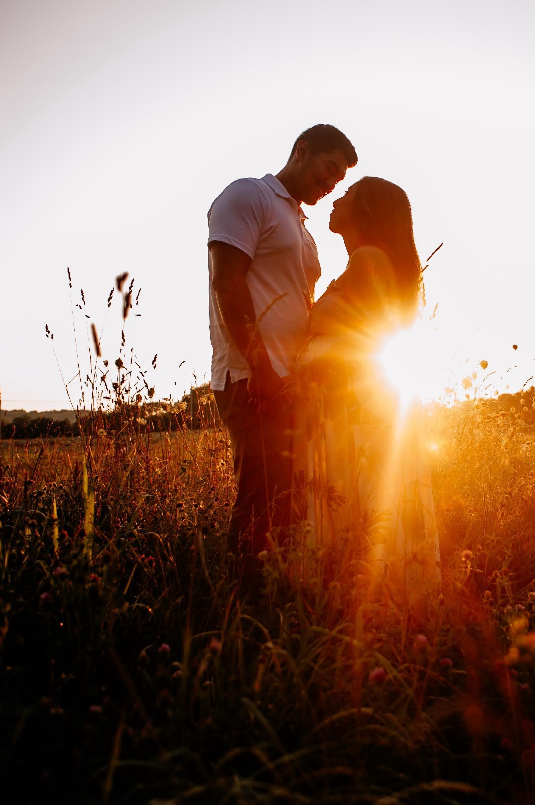 A man and a woman are standing in a field at sunset.
