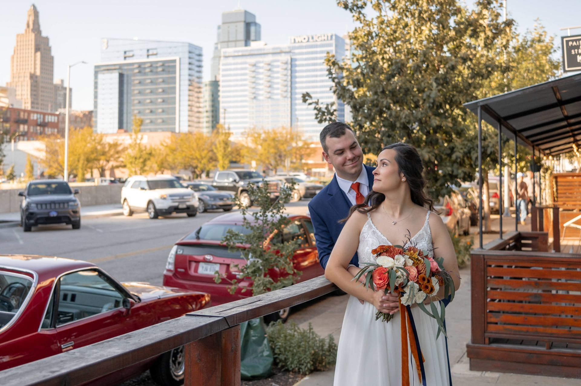 A bride and groom are standing on a balcony overlooking a city street.