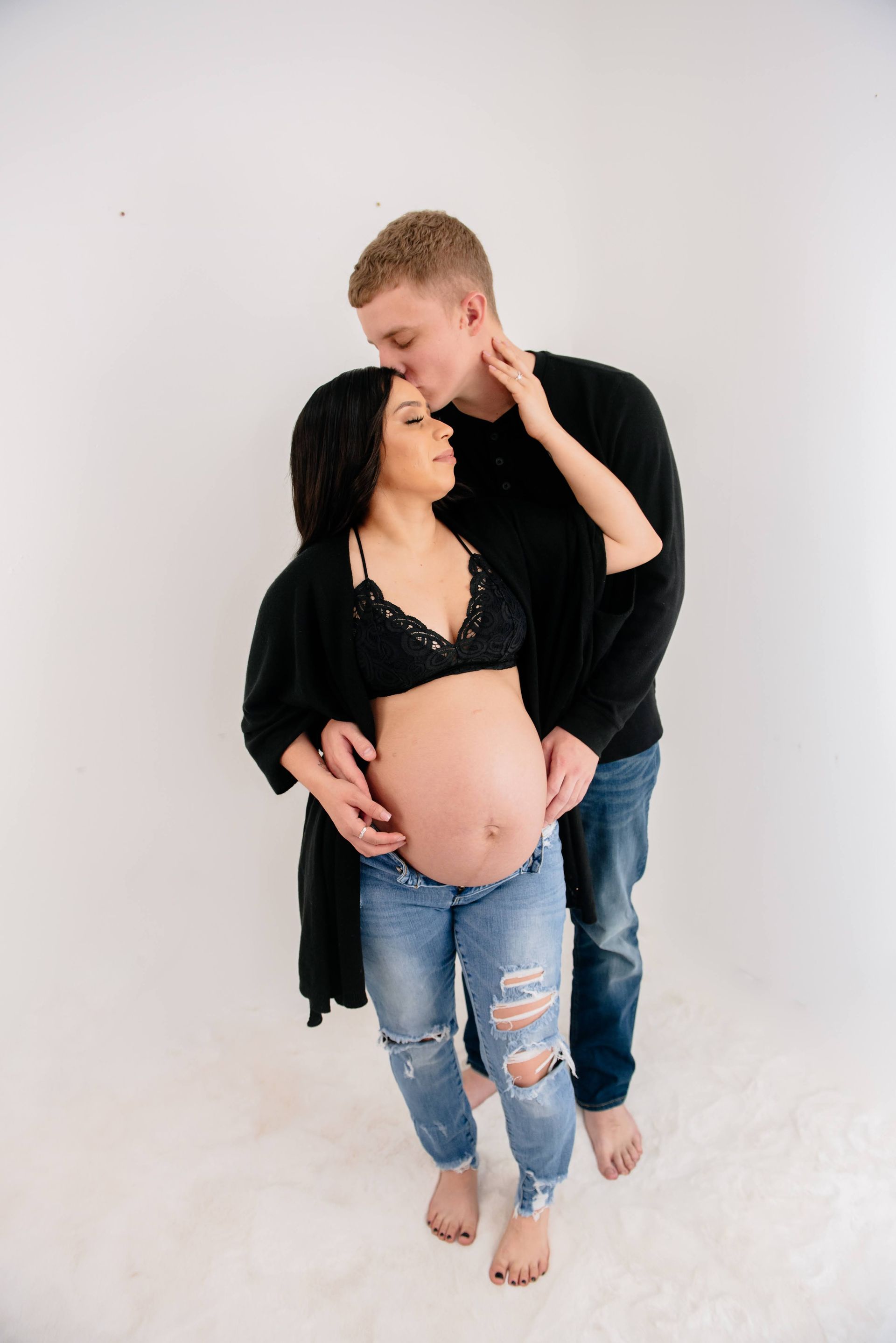 A man is kissing a pregnant woman on the cheek.
