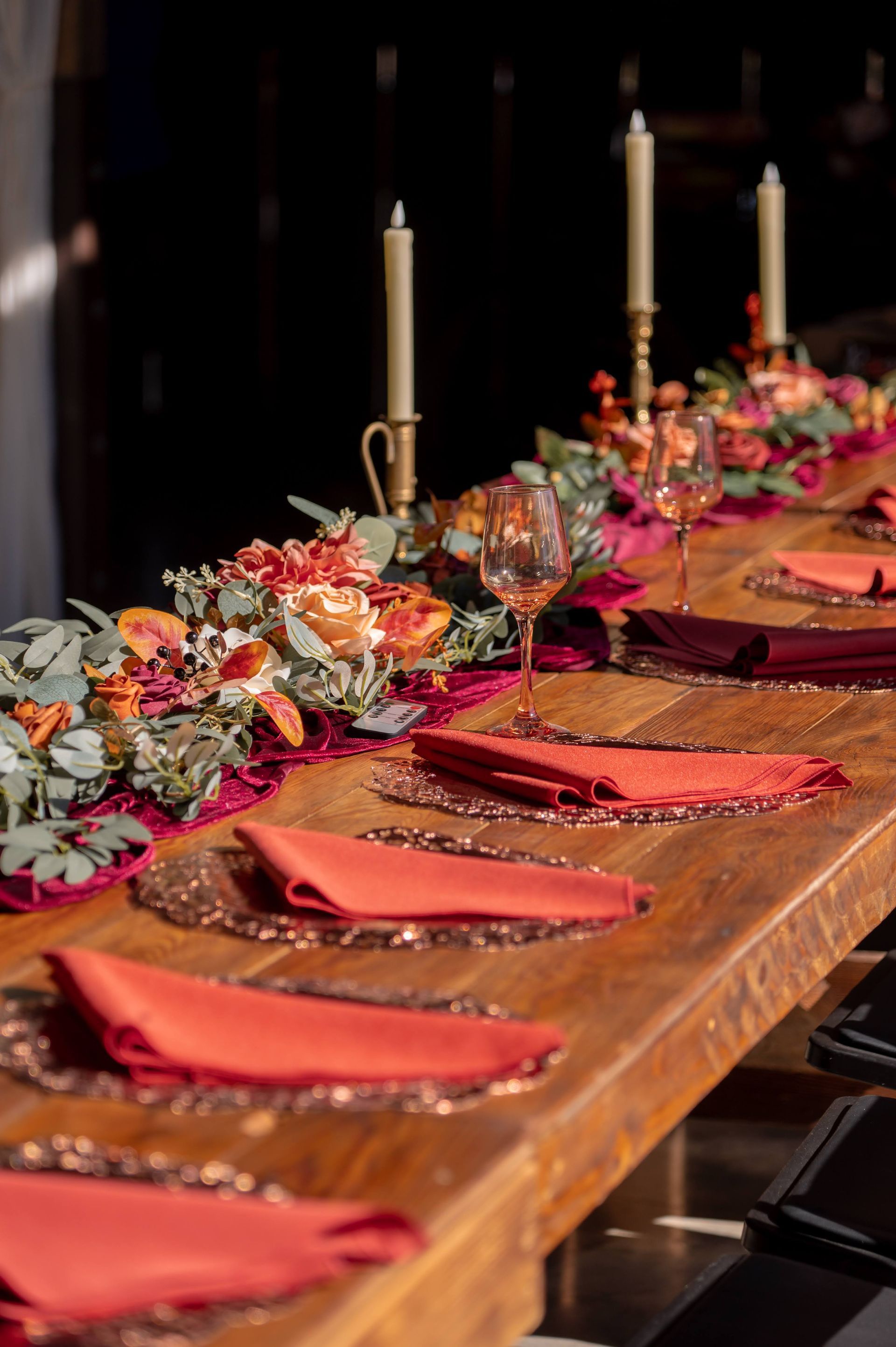 A long wooden table with red napkins and candles on it.