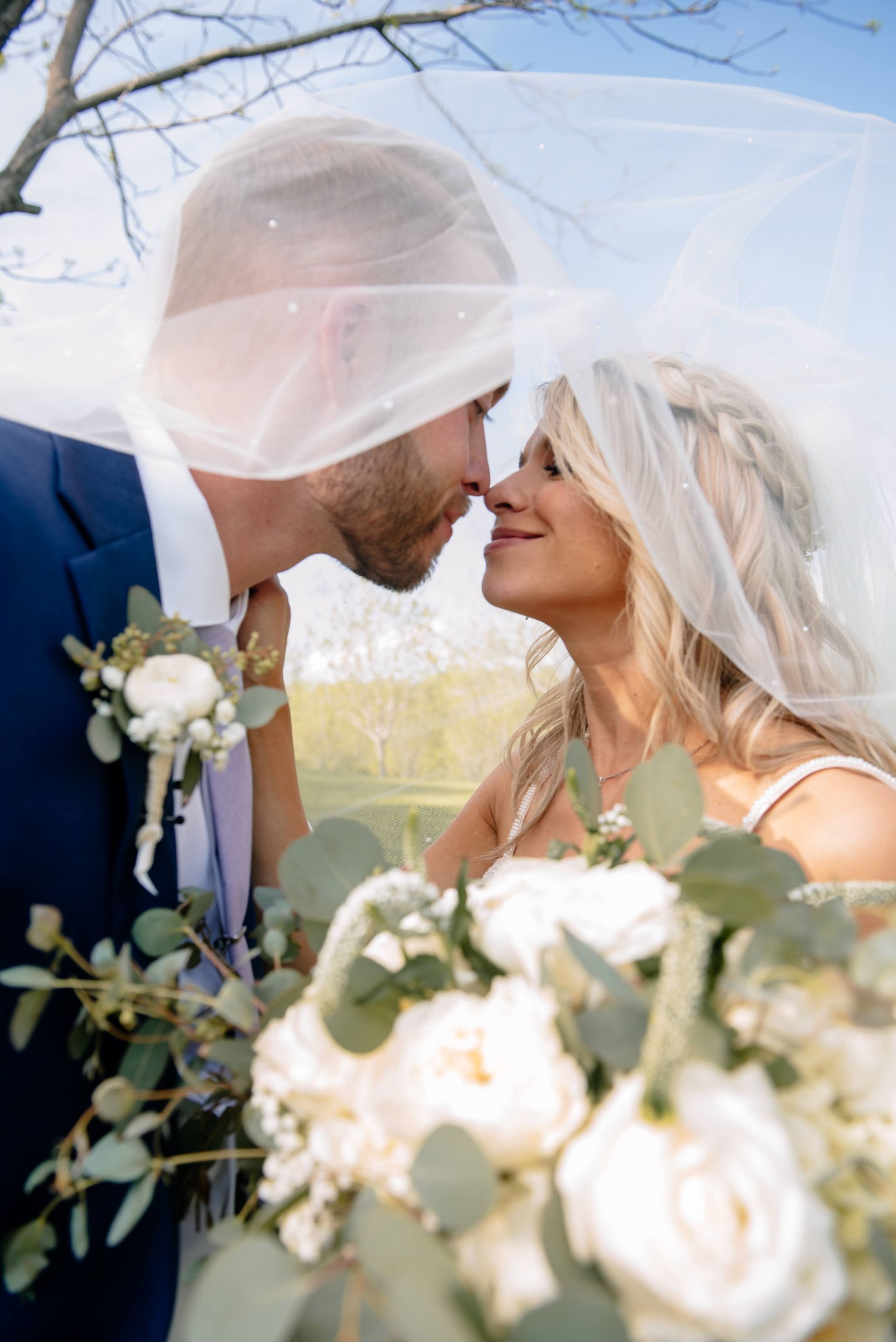 A bride and groom are kissing under a veil.