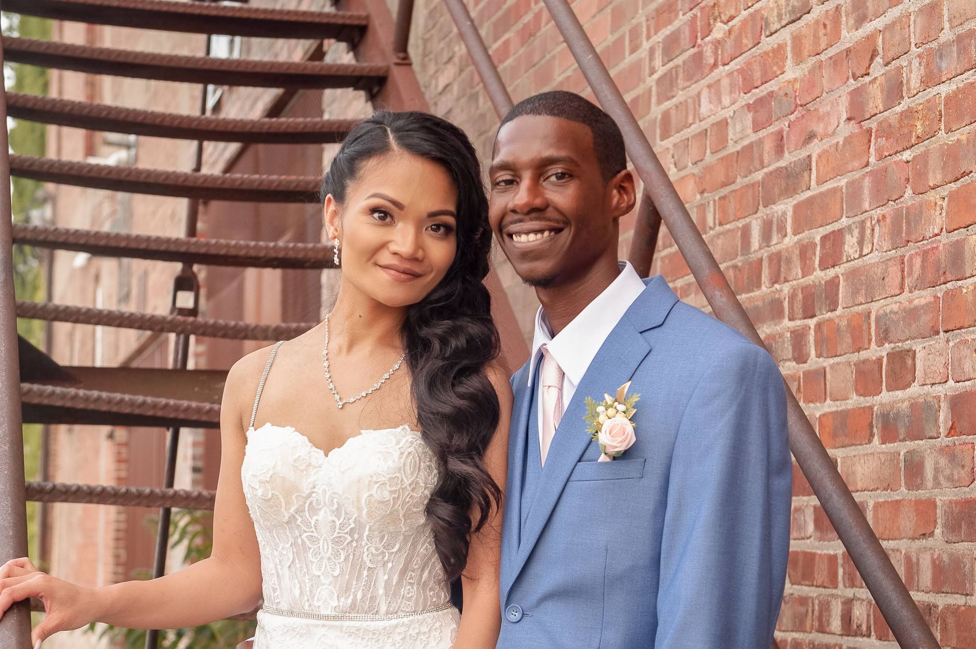 A bride and groom are posing for a picture in front of a fire escape.
