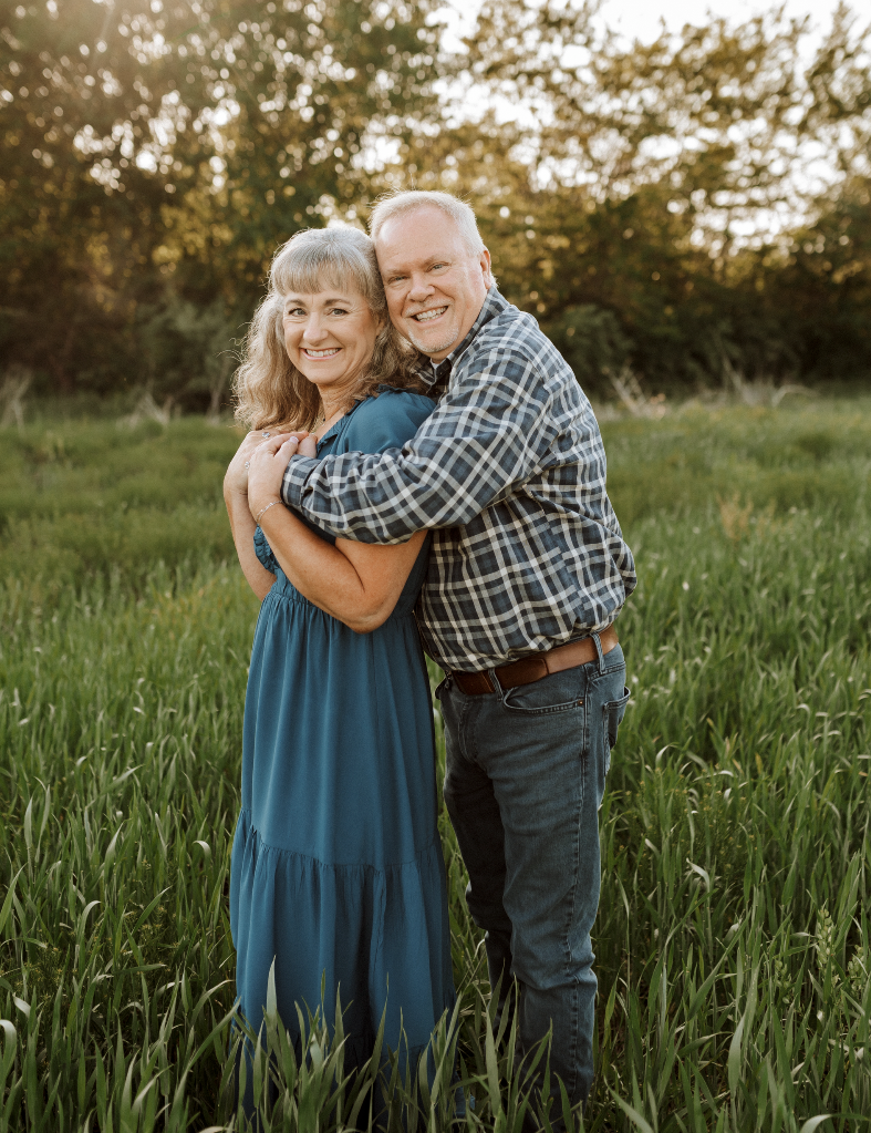 A man and a woman are hugging each other in a field.