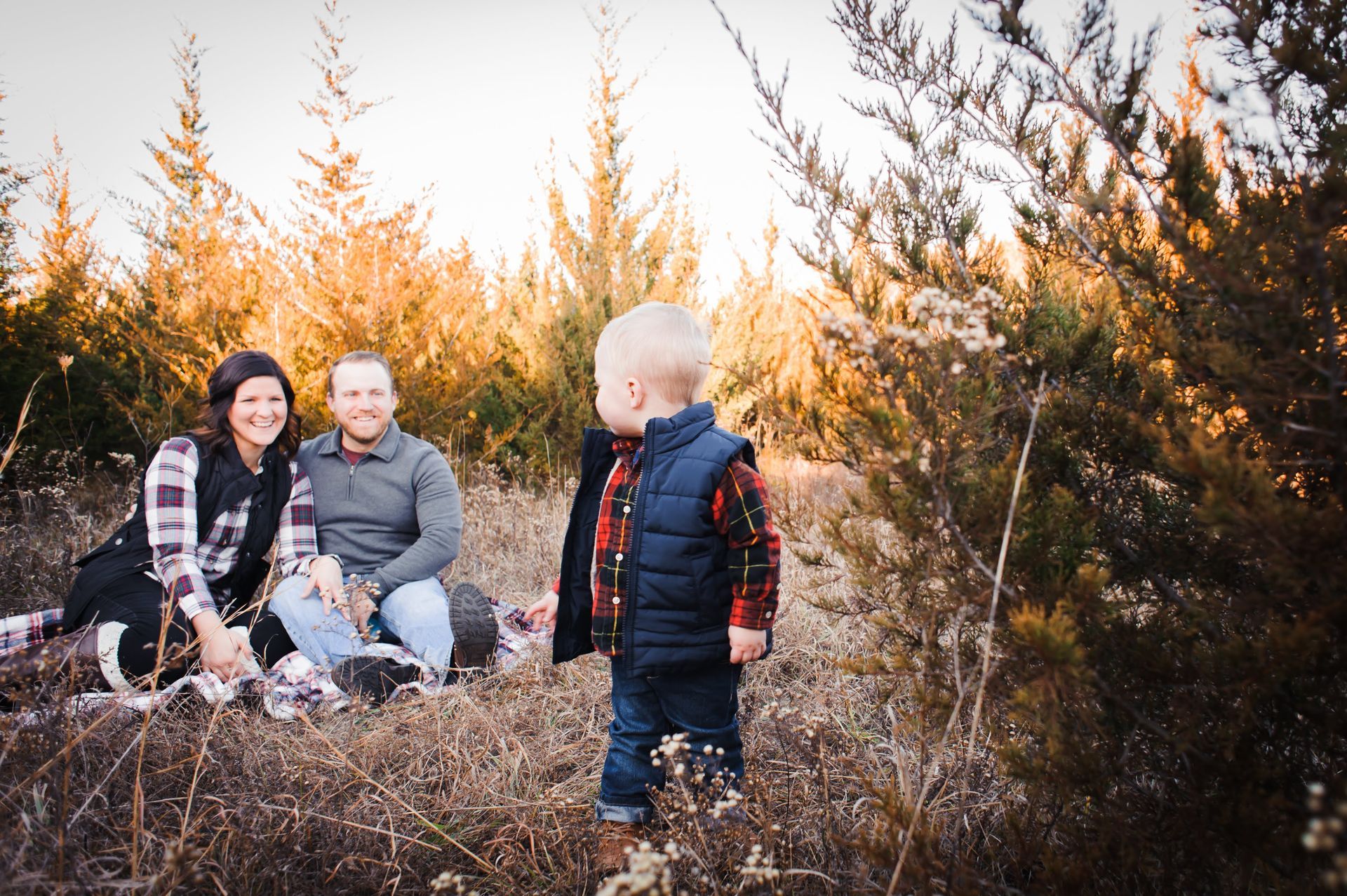 A family is sitting on a blanket in a field with trees in the background.