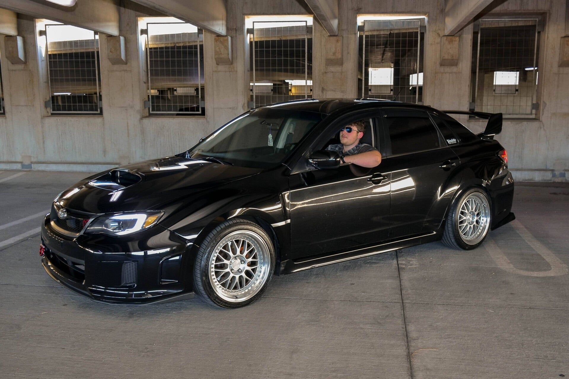 A man is sitting in a black car in a parking garage.