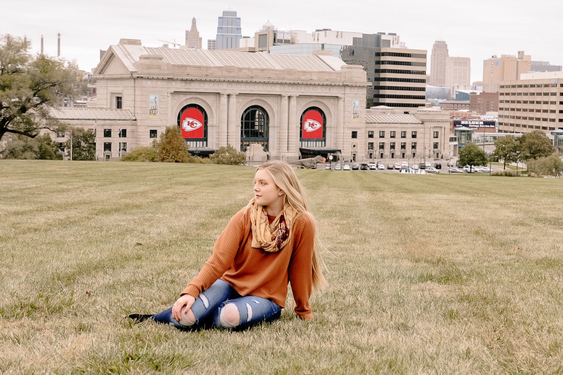 A woman is sitting on the grass in front of a building.