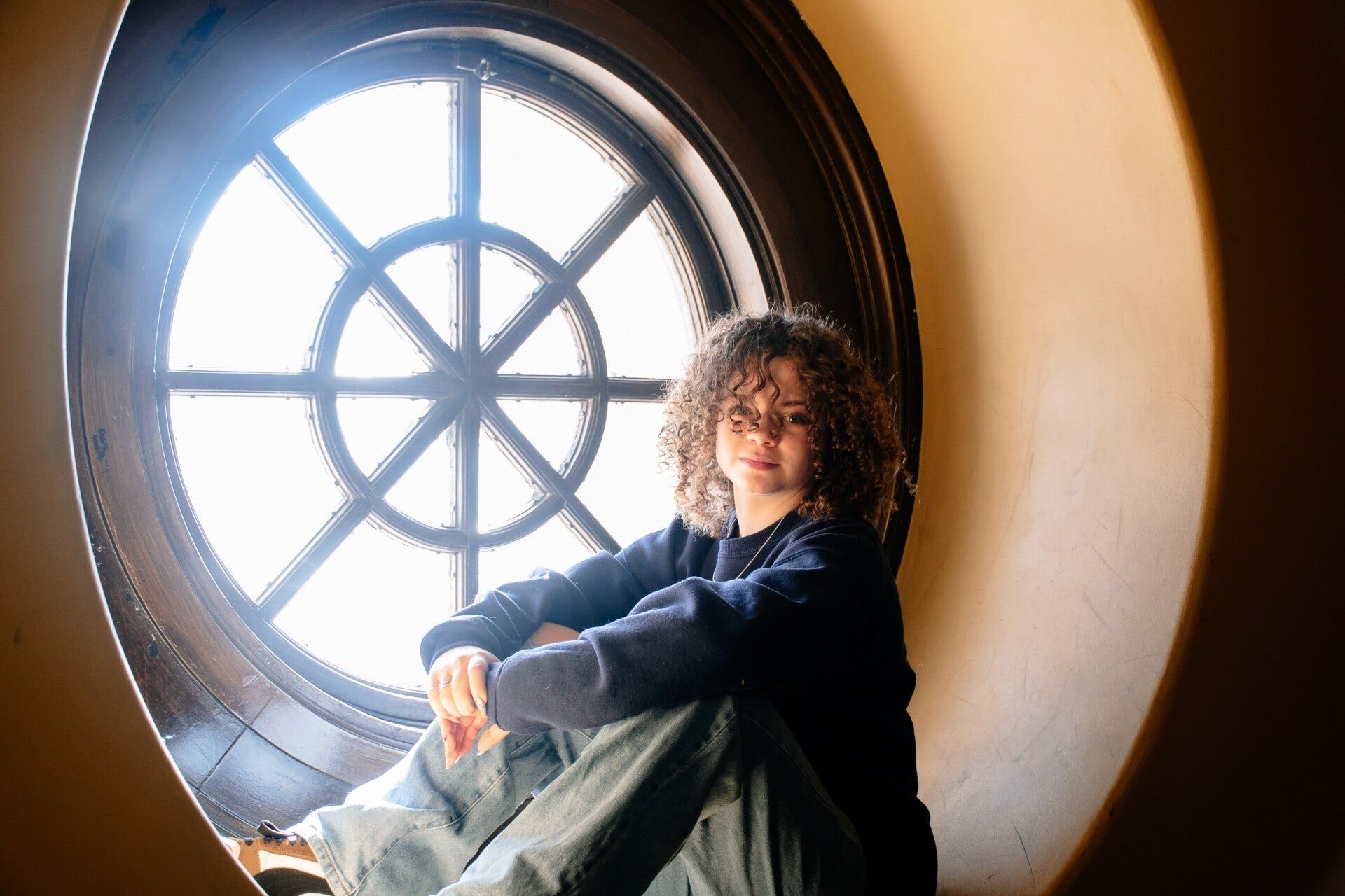 A woman is sitting in a round window looking out.