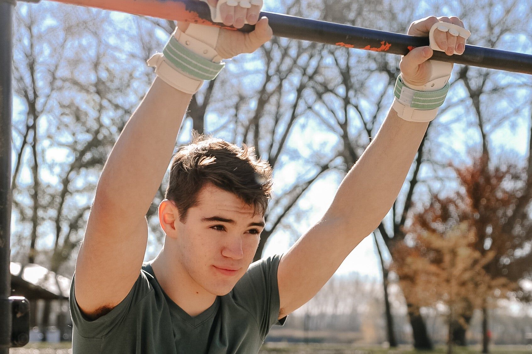 A young man is doing pull ups on a bar in a park.