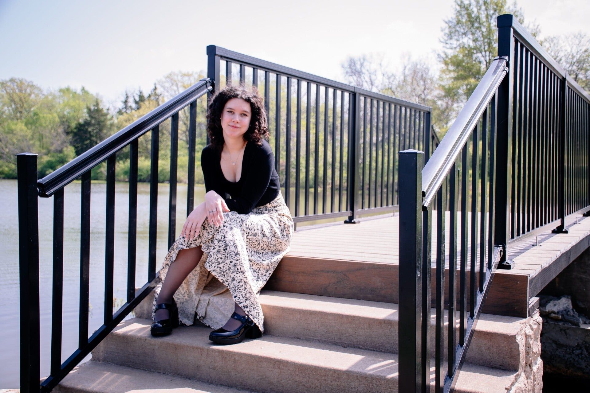 A woman is sitting on the steps of a bridge over a body of water.