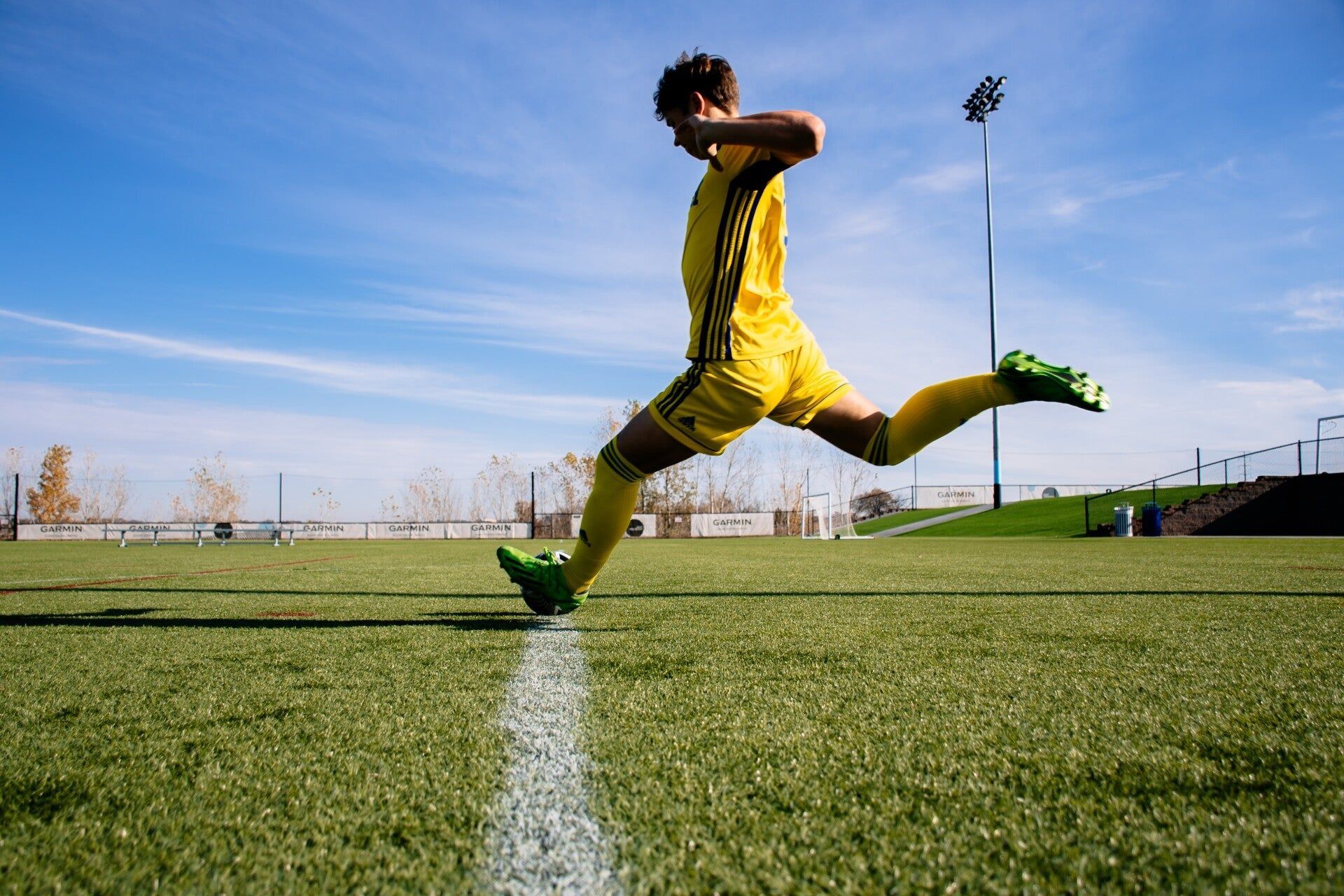 A soccer player is jumping in the air while kicking a soccer ball on a field.